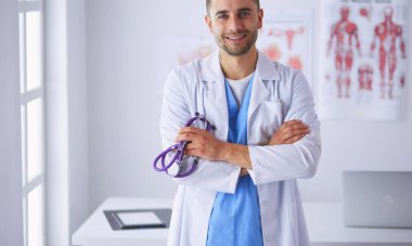 Genç ve kendinden emin erkek doktor portresi tıp ofisinde duruyor..