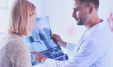 Yakışıklı doktor genç bayan hastasıyla konuşuyor ve ofisinde otururken notlar alıyor..