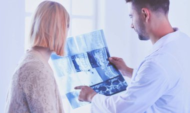 Yakışıklı doktor genç bayan hastasıyla konuşuyor ve ofisinde otururken notlar alıyor..