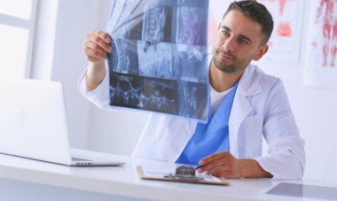 Yakışıklı doktor genç bayan hastasıyla konuşuyor ve ofisinde otururken notlar alıyor..