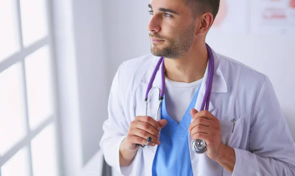 Retrato médico masculino joven y confiado de pie en el consultorio médico. —  Fotos de Stock