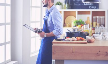 Dijital tablet ve yemek pişirme tarifine uyan bir adam evdeki mutfakta lezzetli ve sağlıklı yemekler pişiriyor.