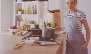 Mutfakta yemek yapmak için tablet bilgisayar kullanan genç bir kadın.