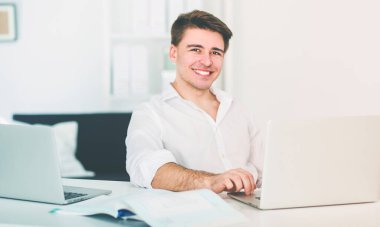 Genç adam sandalyede oturuyor ve dizüstü bilgisayarla çalışıyor.