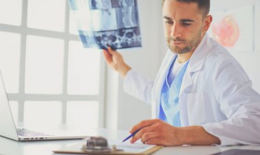 Genç doktor ofisinde oturuyor ve röntgen sonuçlarını inceliyor.