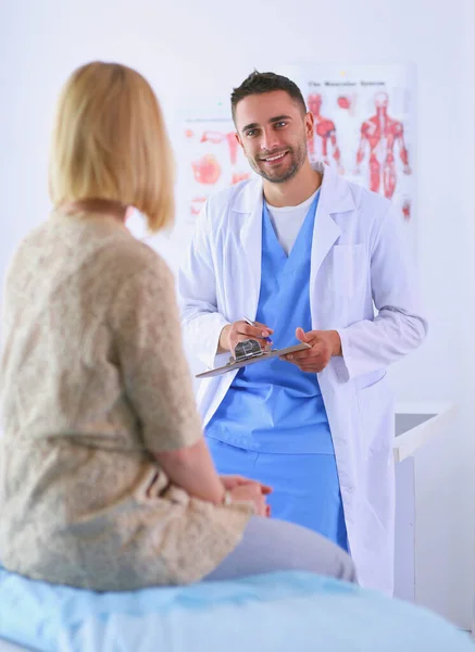 El guapo doctor está hablando con una paciente joven y tomando notas mientras está sentado en su consultorio. —  Fotos de Stock