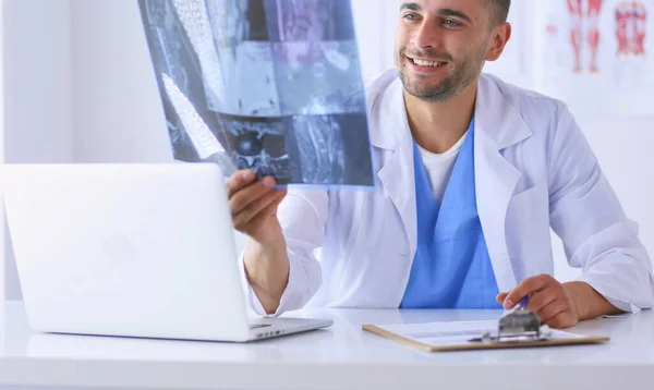 Jovem médico sentado em sua mesa de escritório e analisando um raio-x — Fotografia de Stock