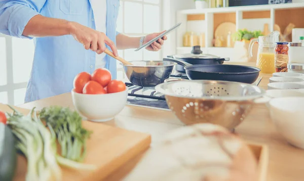 Man following recipe on digital tablet and cooking tasty and healthy food in kitchen at home — Stock Photo, Image