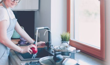 Sebze yıkayan kadın. Güzel genç bir kadın salata için sebze yıkıyor ve mutfakta dururken gülümsüyor.