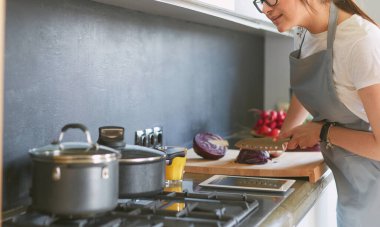 Mutfakta yemek yapmak için tablet bilgisayar kullanan genç bir kadın.