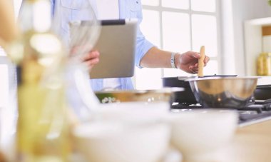 Dijital tablet ve yemek pişirme tarifine uyan bir adam evdeki mutfakta lezzetli ve sağlıklı yemekler pişiriyor.