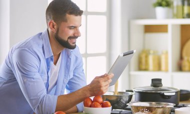 Dijital tablet ve yemek pişirme tarifine uyan bir adam evdeki mutfakta lezzetli ve sağlıklı yemekler pişiriyor.