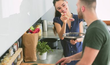 Bir çift evdeki mutfaklarında birlikte yemek pişiriyor.