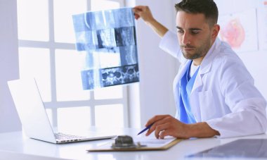 Yakışıklı doktor genç bayan hastasıyla konuşuyor ve ofisinde otururken notlar alıyor..