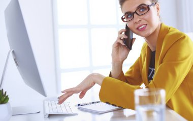 İş kadını ofiste bilgisayar ve cep telefonu kullanarak işine konsantre oluyor.