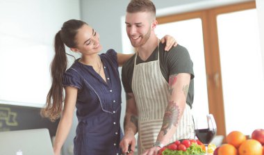 Sebze doğrayan genç bir adam ve mutfakta dizüstü bilgisayarı olan bir kadın.