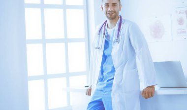 Genç ve kendinden emin erkek doktor portresi tıp ofisinde duruyor..