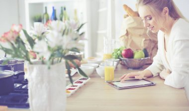 Mutfakta dijital tablet kullanan güzel genç bir kadın.