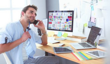 İnternette çalışırken bilgisayarın ve dizüstü bilgisayarın önünde grafik stüdyosunda oturan genç tasarımcının portresi.