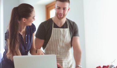 Sebze doğrayan genç bir adam ve mutfakta dizüstü bilgisayarı olan bir kadın.