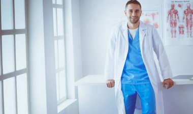 Genç ve kendinden emin erkek doktor portresi tıp ofisinde duruyor.