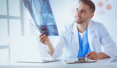 Genç doktor ofisinde oturuyor ve röntgen sonuçlarını inceliyor.