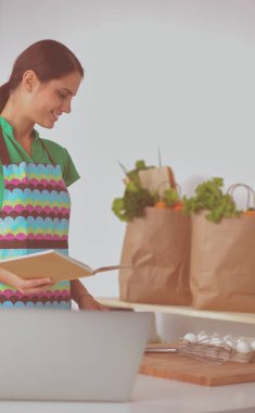 Güzel bir kadın mutfakta dizüstü bilgisayarıyla rahatlarken bir fincan kahvenin tadını çıkarıyor.