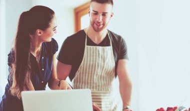 Sebze doğrayan genç bir adam ve mutfakta dizüstü bilgisayarı olan bir kadın.