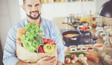 Mutfak arka planında poşet dolusu erzak tutan adam. Alışveriş ve sağlıklı gıda konsepti