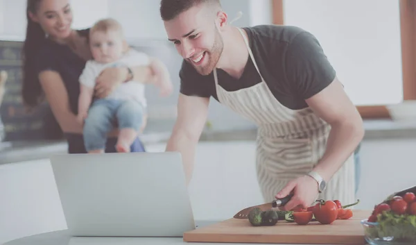 Retrato del hombre cocinando verduras en la cocina mientras mira una computadora portátil en la mesa — Foto de Stock