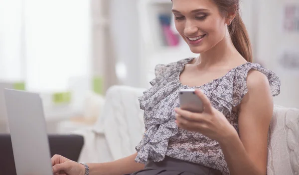 Jonge lachende mooie vrouw die zit op de Bank met telefoon en laptop — Stockfoto