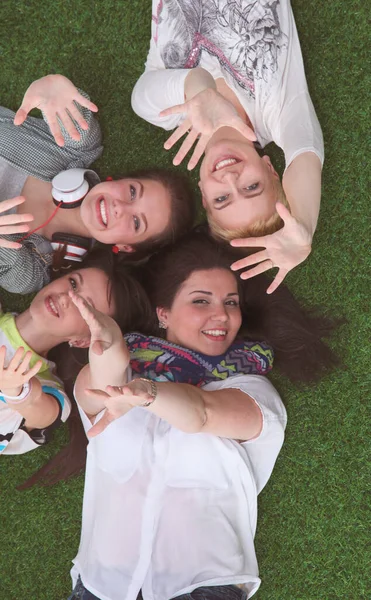 Quatre jeunes femmes allongées sur de l'herbe verte les mains en l'air — Photo