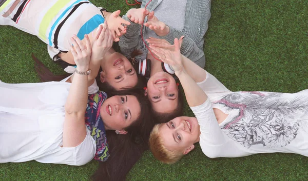 Quatre jeunes femmes allongées sur de l'herbe verte les mains en l'air — Photo