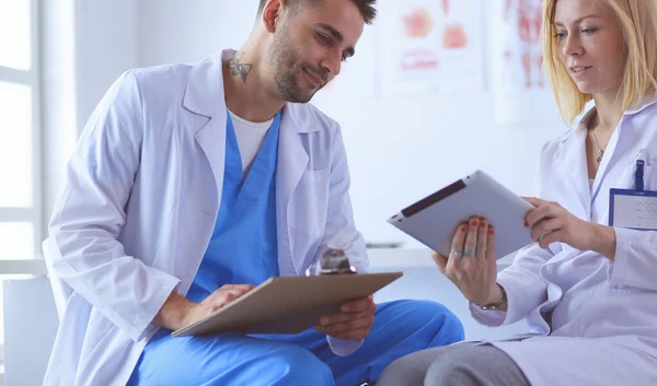 El guapo doctor está hablando con una paciente joven y tomando notas mientras está sentado en su consultorio. —  Fotos de Stock