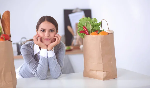 Giovane donna che tiene la borsa della spesa con verdure. In piedi in cucina — Foto Stock