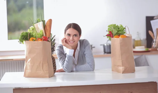 Mujer joven sosteniendo bolsa de la compra de comestibles con verduras. De pie en la cocina —  Fotos de Stock