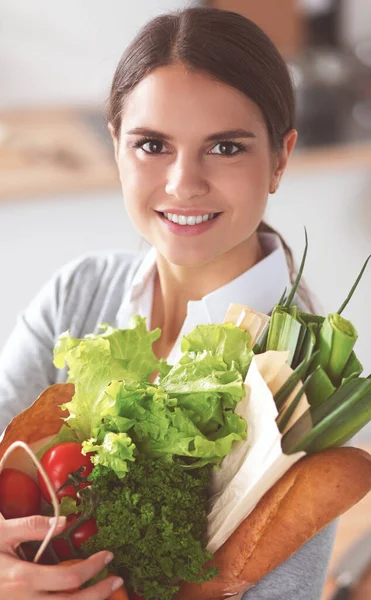 Mladá žena držící nákupní tašku se zeleninou Stojící v kuchyni — Stock fotografie