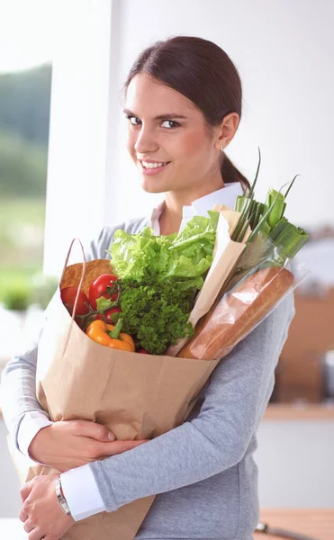 Νεαρή γυναίκα κρατάει τσάντα για ψώνια με λαχανικά. Στέκεται στην κουζίνα. — Φωτογραφία Αρχείου