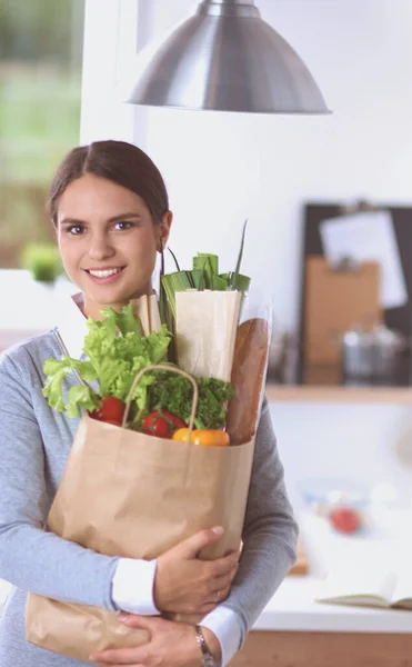 Giovane donna che tiene la spesa con verdure In piedi in cucina. — Foto Stock