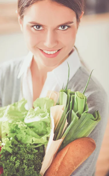 Mujer joven sosteniendo bolsa de la compra de comestibles con verduras. De pie en la cocina — Foto de Stock