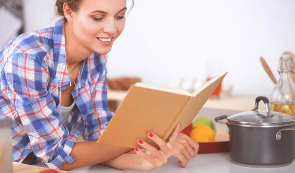 Jovem mulher lendo livro de receitas na cozinha, à procura de receita — Fotografia de Stock