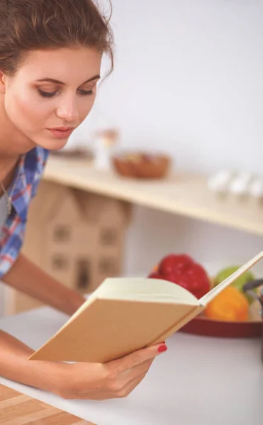 Jovem mulher lendo livro de receitas na cozinha, à procura de receita — Fotografia de Stock