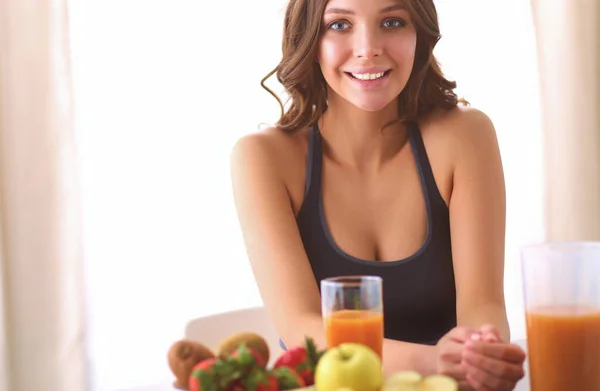 Chica sentada en la cocina en el escritorio con frutas y vasos con jugo —  Fotos de Stock