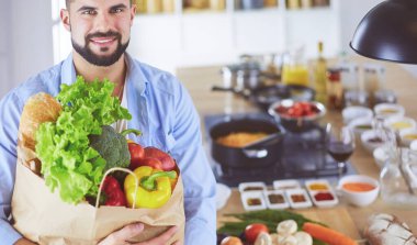 Mutfak arka planında poşet dolusu erzak tutan adam. Alışveriş ve sağlıklı gıda konsepti