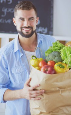 Mutfak arka planında poşet dolusu erzak tutan adam. Alışveriş ve sağlıklı gıda konsepti