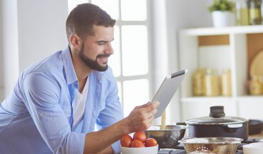 Dijital tablet ve yemek pişirme tarifine uyan bir adam evdeki mutfakta lezzetli ve sağlıklı yemekler pişiriyor.