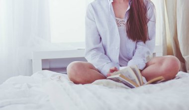 Yatakta oturup kitap okuyan ve kahvaltı yapan bir kadın.