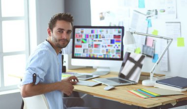 İnternette çalışırken bilgisayarın ve dizüstü bilgisayarın önünde grafik stüdyosunda oturan genç tasarımcının portresi.