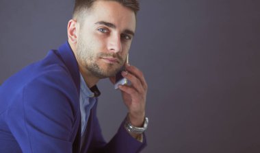 Gri arka planda yalnız oturan genç iş adamı.