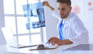 Yakışıklı doktor genç bayan hastasıyla konuşuyor ve ofisinde otururken notlar alıyor..